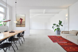 Modernes Tageslicht-Mietstudio in Berlin für Foto- und Videoproduktionen in heller Loft-Atmosphäre mit Studiobeleuchtung, Holztisch, Sofa, großem Fenster und minimalistischer Einrichtung.